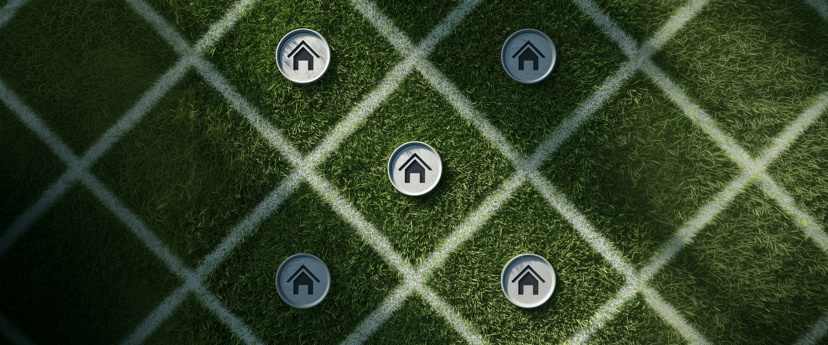 Symbolische Darstellung mit Haus-Icons auf einem rasterförmig markierten Rasen. Konzeptbild zur Frage „Was kostet ein Quadratmeter Hausbau?“